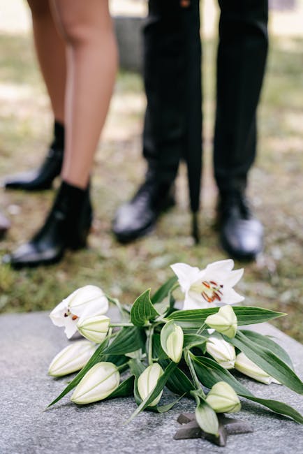 A delicate floral arrangement composed of white lilies with their large, trumpet-shaped petals and prominent stamens, paired with several unopened lily buds and long, slender green leaves, all placed